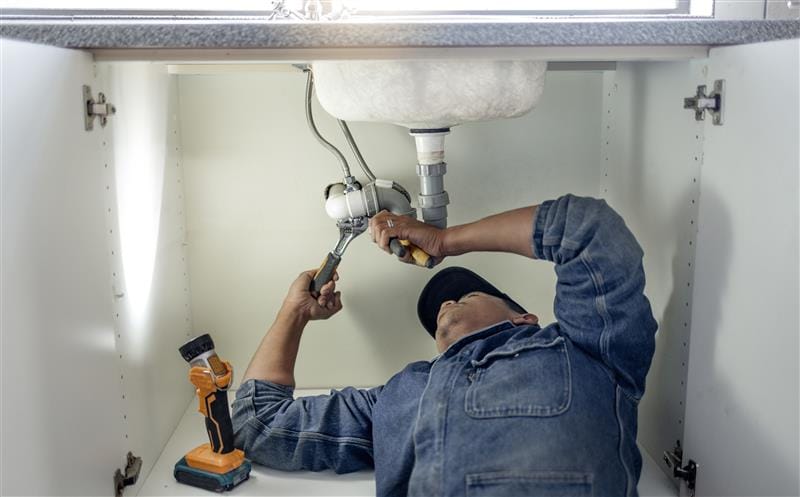 Plumber repairing pipes beneath a bathroom sink in Kissimmee