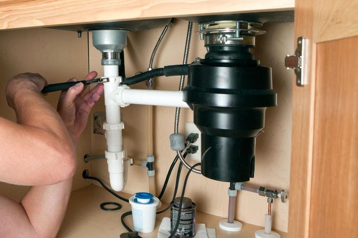 Plumber installing a garbage disposal beneath a kitchen sink in Kissimmee