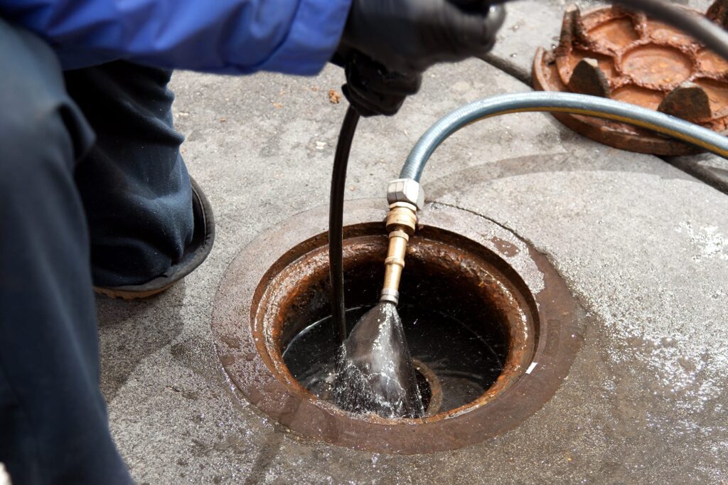 Plumber hydro jetting a sewer line through a manhole in Kissimmee