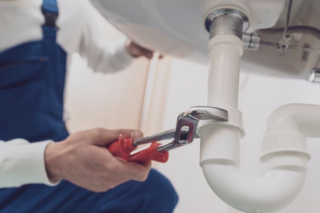 Plumber repairing a white drain pipe beneath a sink in Kissimmee